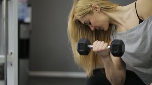 The girl performs a dumbbell workout